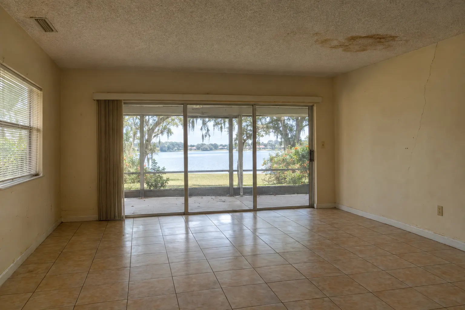 Example image, not one of our jobs: a dated living room with a water-stained popcorn ceiling, a cracked wall, scuffed paint and old tile floor.