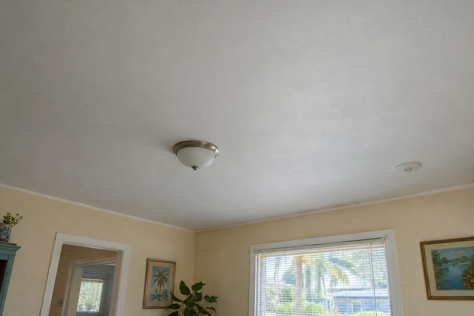 Example image, not one of our jobs: a smooth, freshly painted white ceiling with a simple light fixture, meeting cream walls in a clean corner.