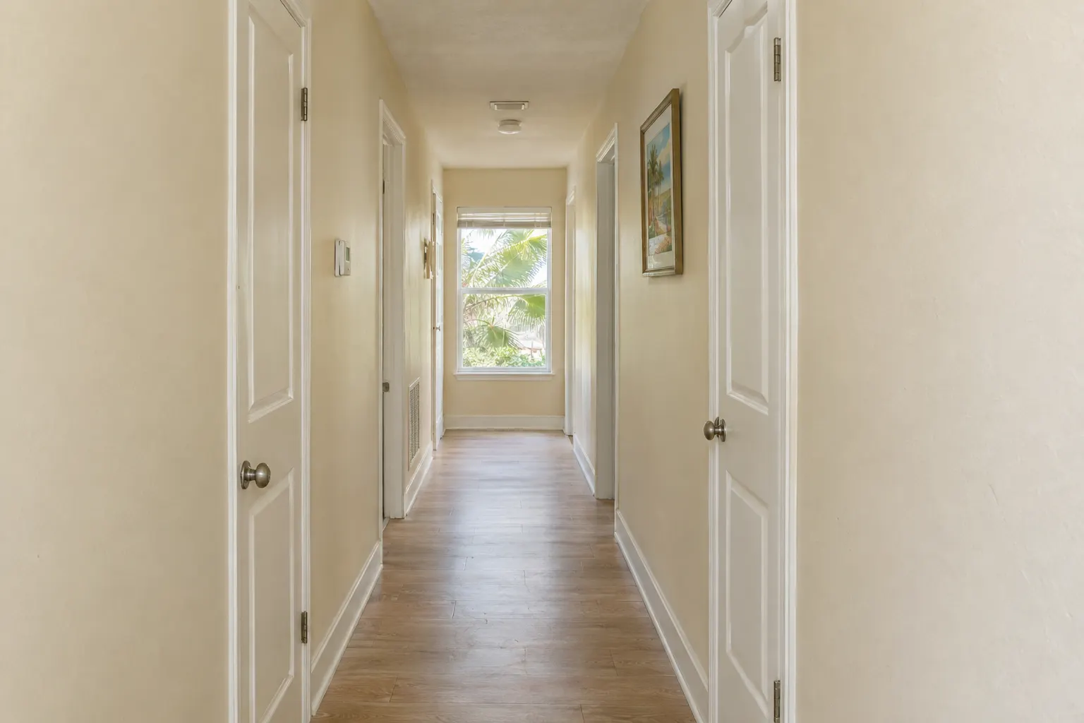 Example image, not one of our jobs: a renovated hallway in a Florida ranch home with cream walls, white doors and baseboards, a plank floor and a window at the far end.