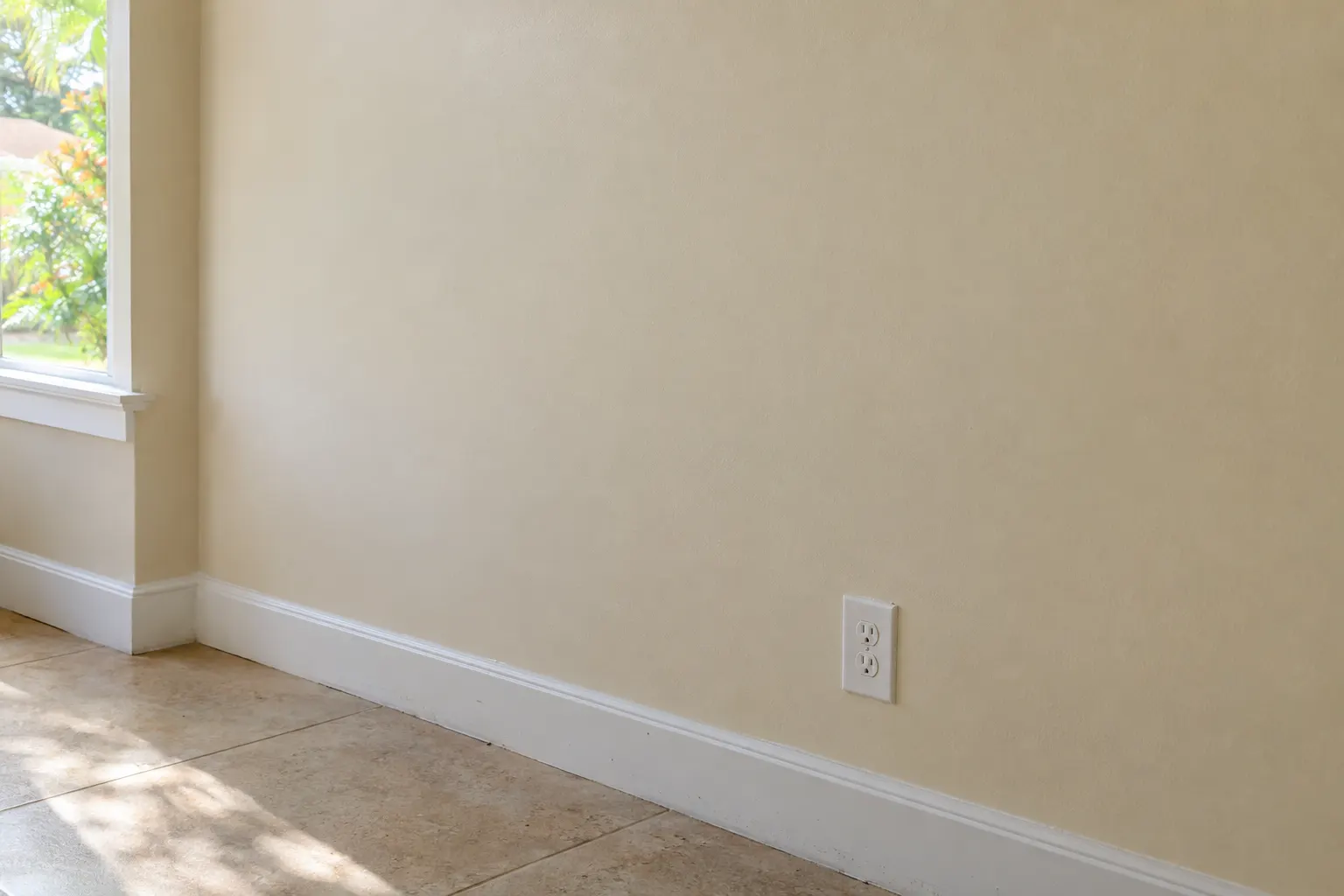 Example image, not one of our jobs: a smooth, freshly painted cream wall with a white baseboard, lit by low daylight from a window that shows no patch or seam.